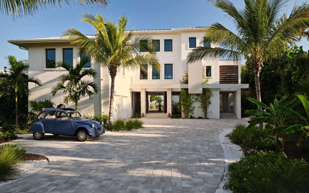 modern two story house with palm trees in front, stone driveway, and a vintage blue car parked on the left side.
